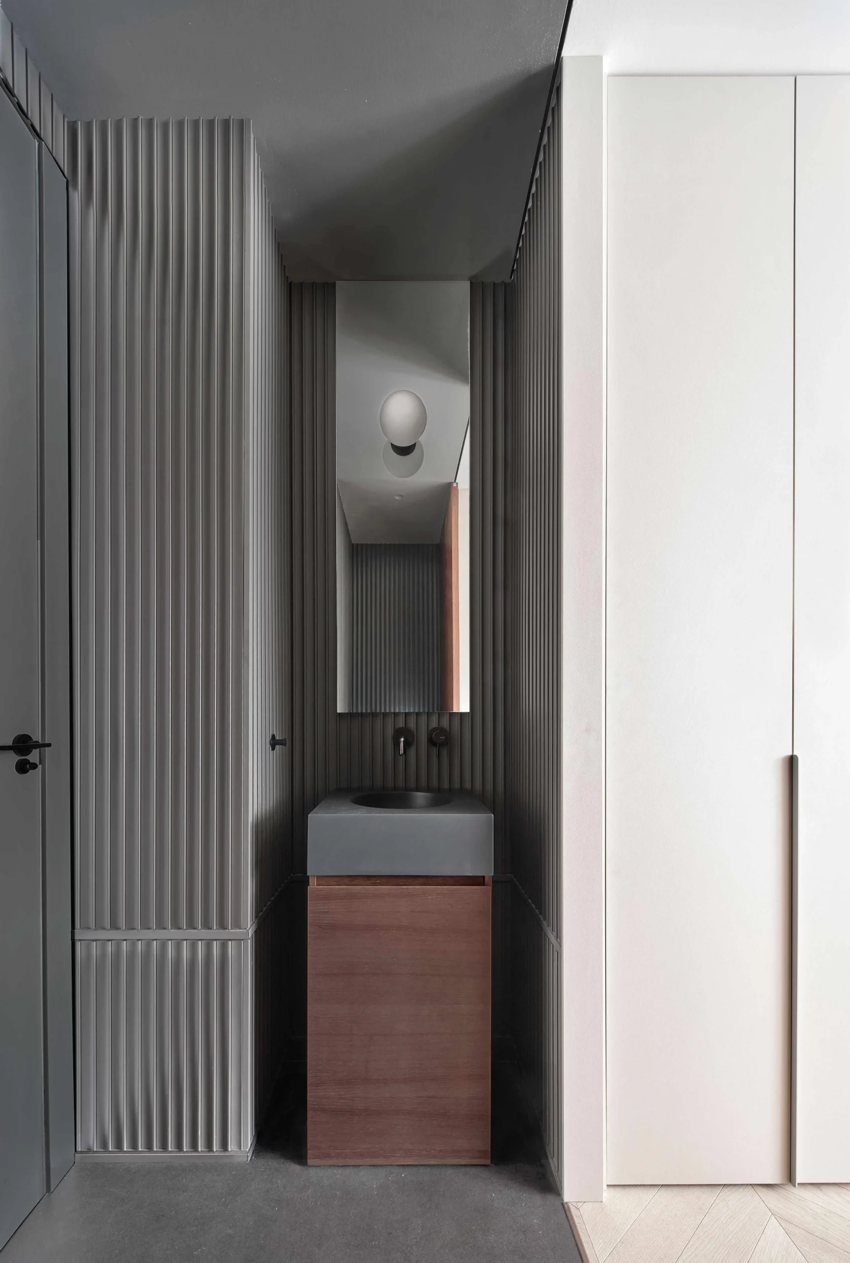 Minimalist bathroom with dark grey concrete sink and ribbed wall panels by Cometa Architects