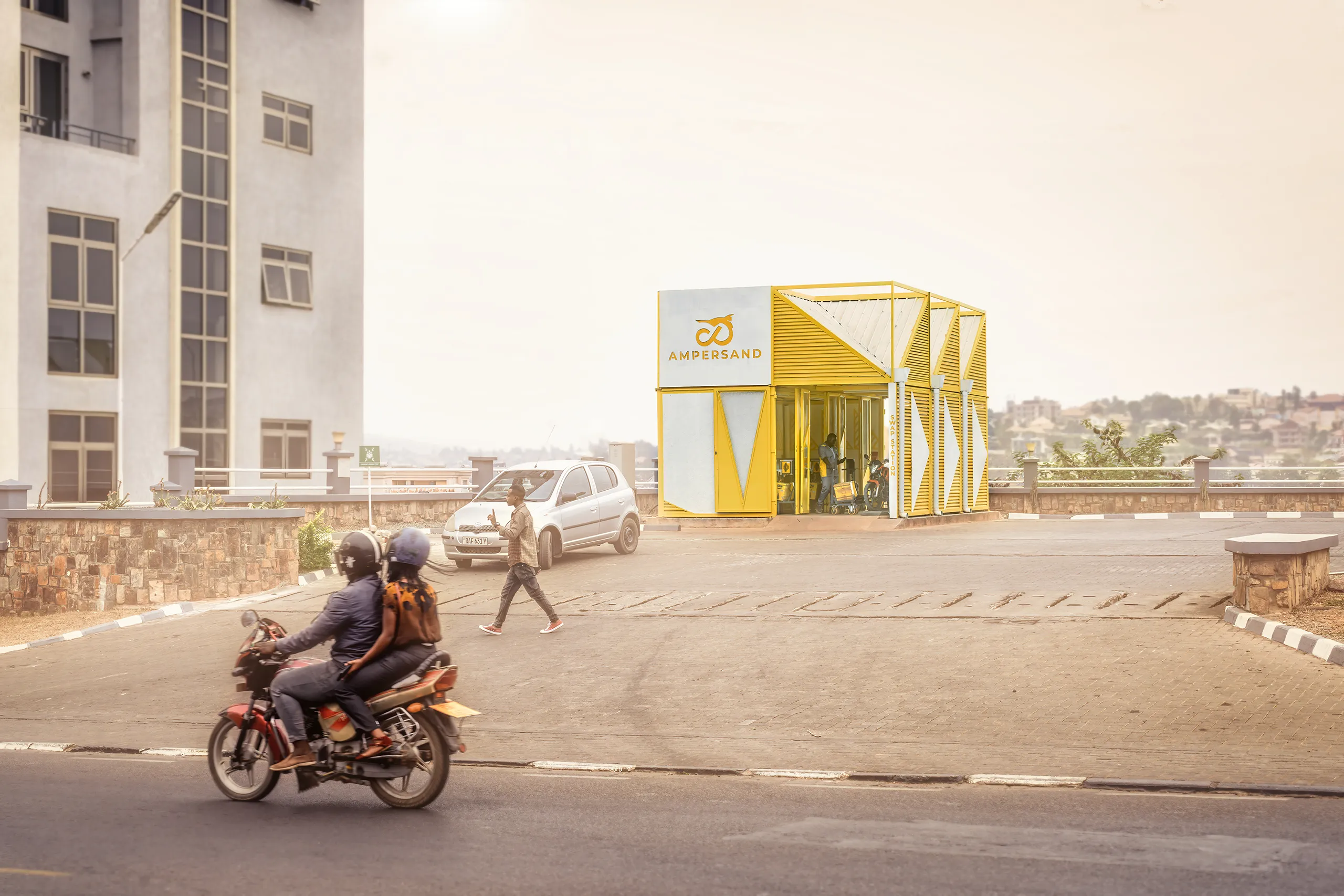 Yellow modular battery swap station for Ampersand in Kigali with passing motorcycle and car.