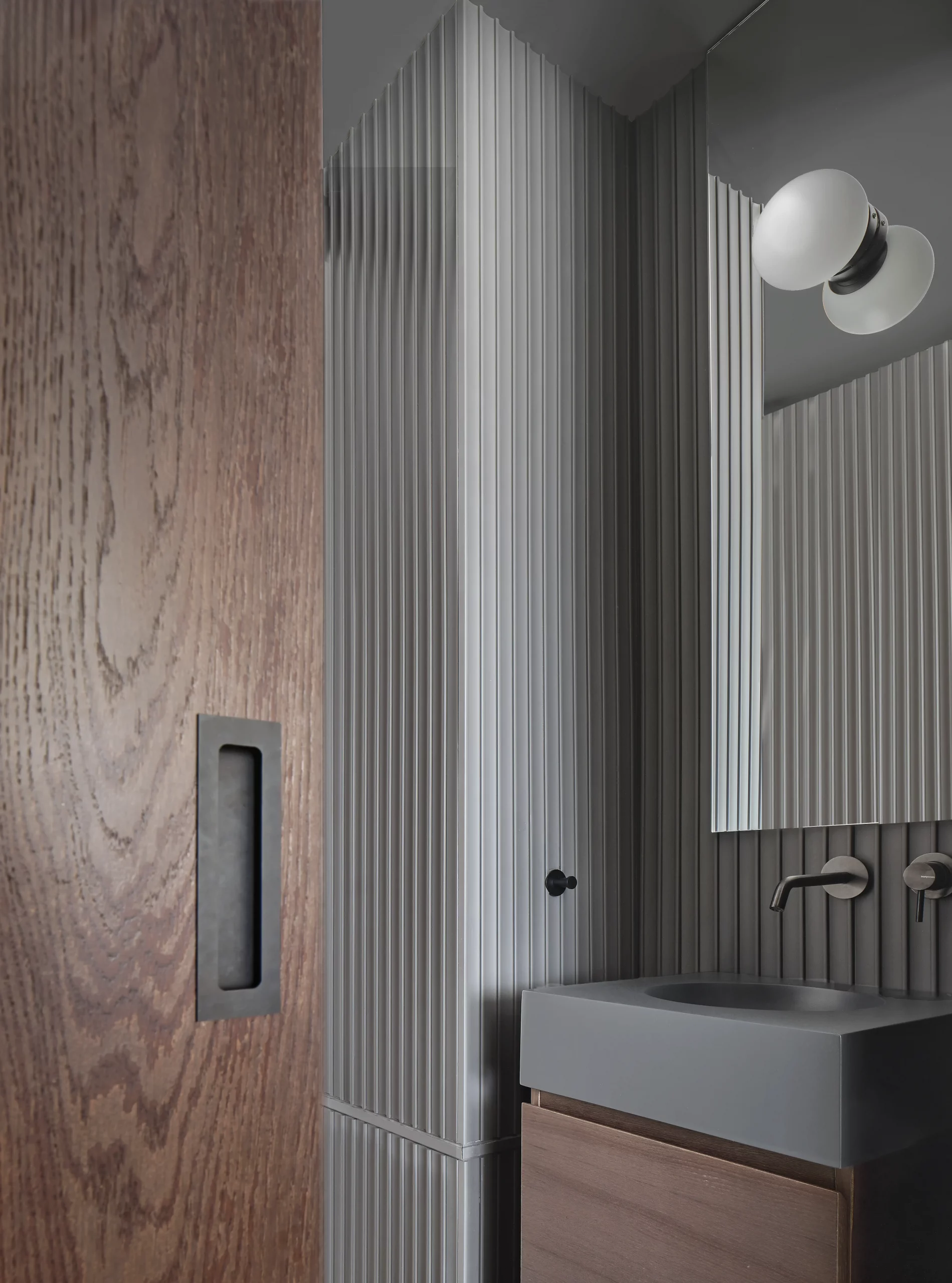 Interior detail of bathroom with ribbed grey wall panels and wooden sliding door by Cometa Architects