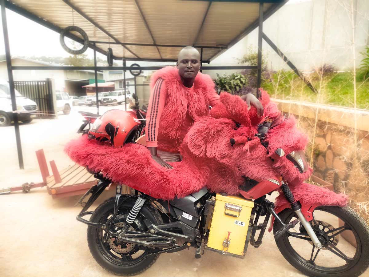Electric motorcycle driver in Kigali wearing bright red fur seat cover and matching vest.