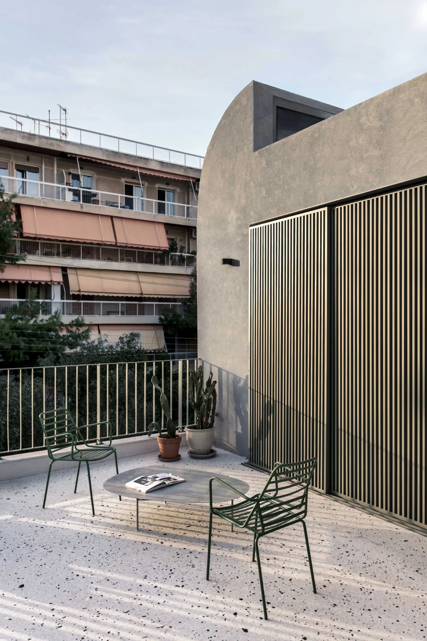 Terrace of Casa D by Cometa Architects in Athens featuring terrazzo flooring, green metal chairs, and minimalist facade with vertical shutters.