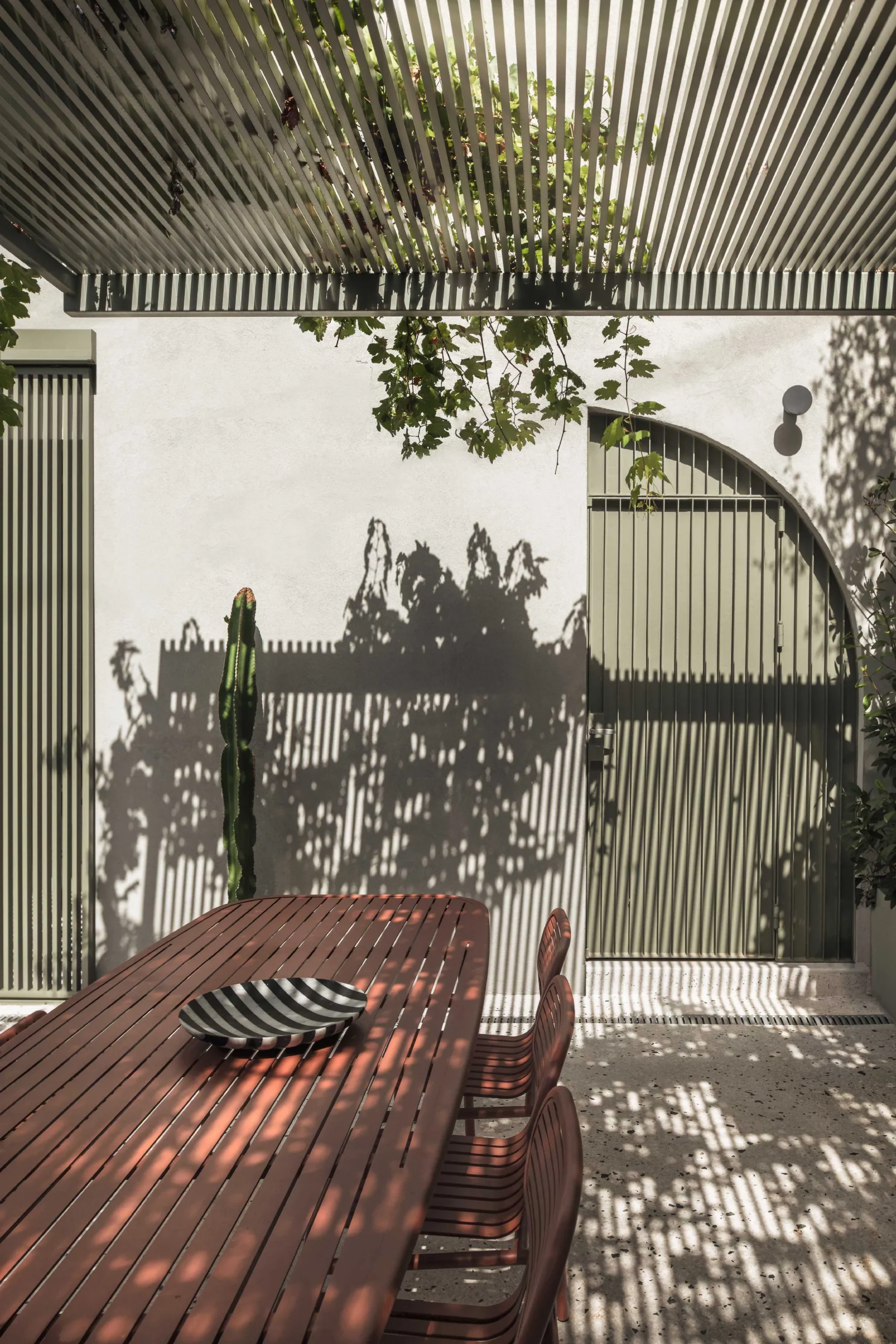 Garden of Casa D by Cometa Architects in Athens featuring terrazzo steps, green metal furniture, terracotta pots, and lush Mediterranean vegetation.