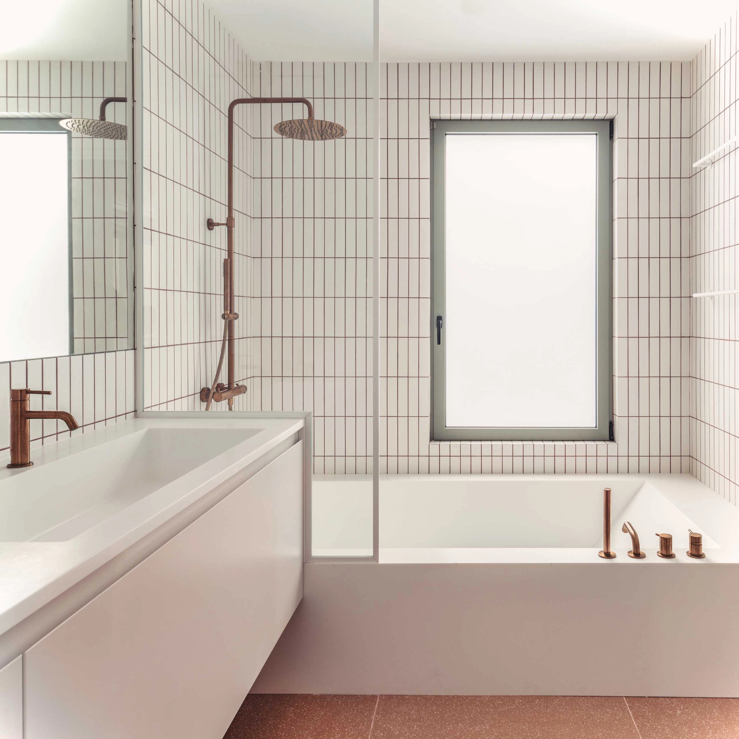 Main bathroom of Casa D by Cometa Architects in Athens with white vertical tiles, copper fixtures, built-in bathtub, and minimalist vanity.