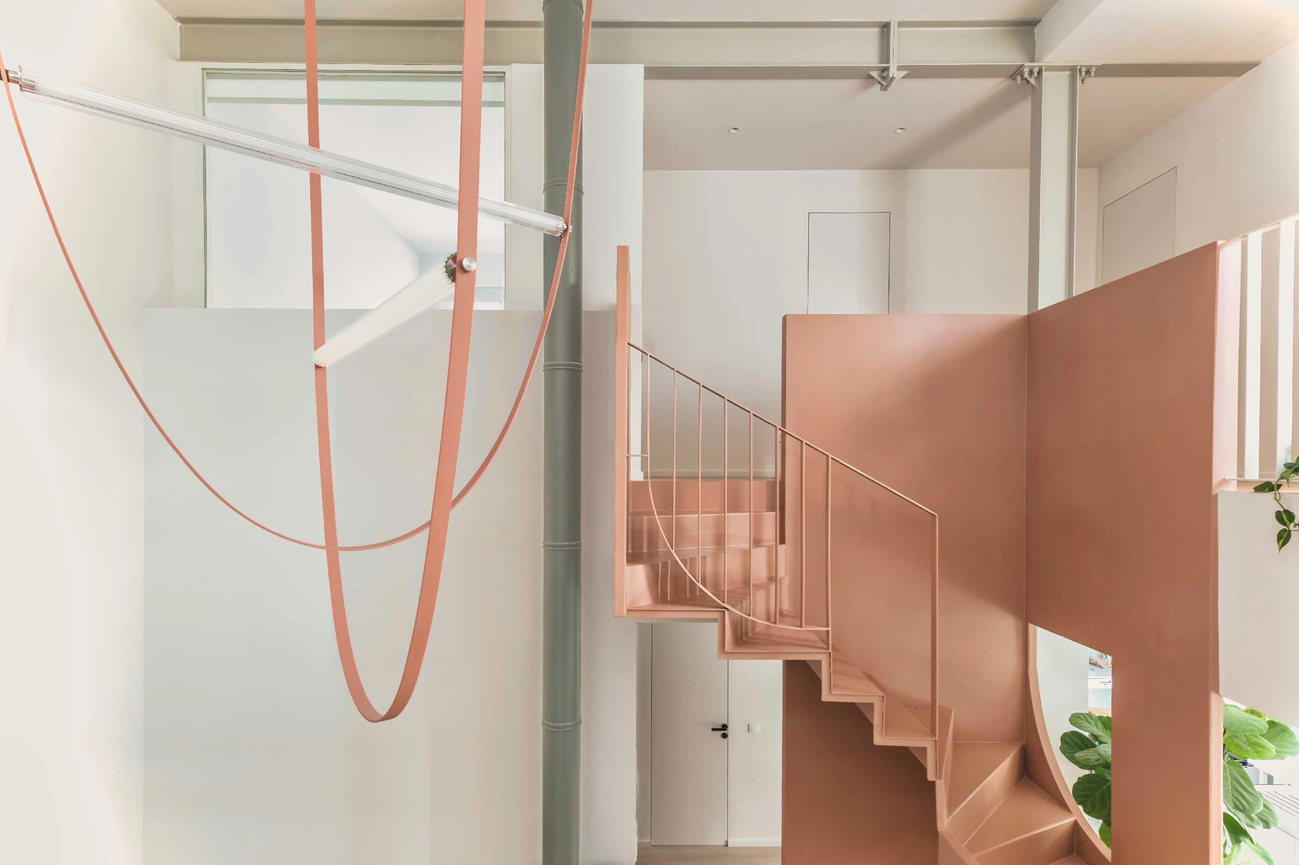 Interior view of Casa D by Cometa Architects in Athens showing a pink steel staircase, sculptural lighting, and exposed structural beams.
