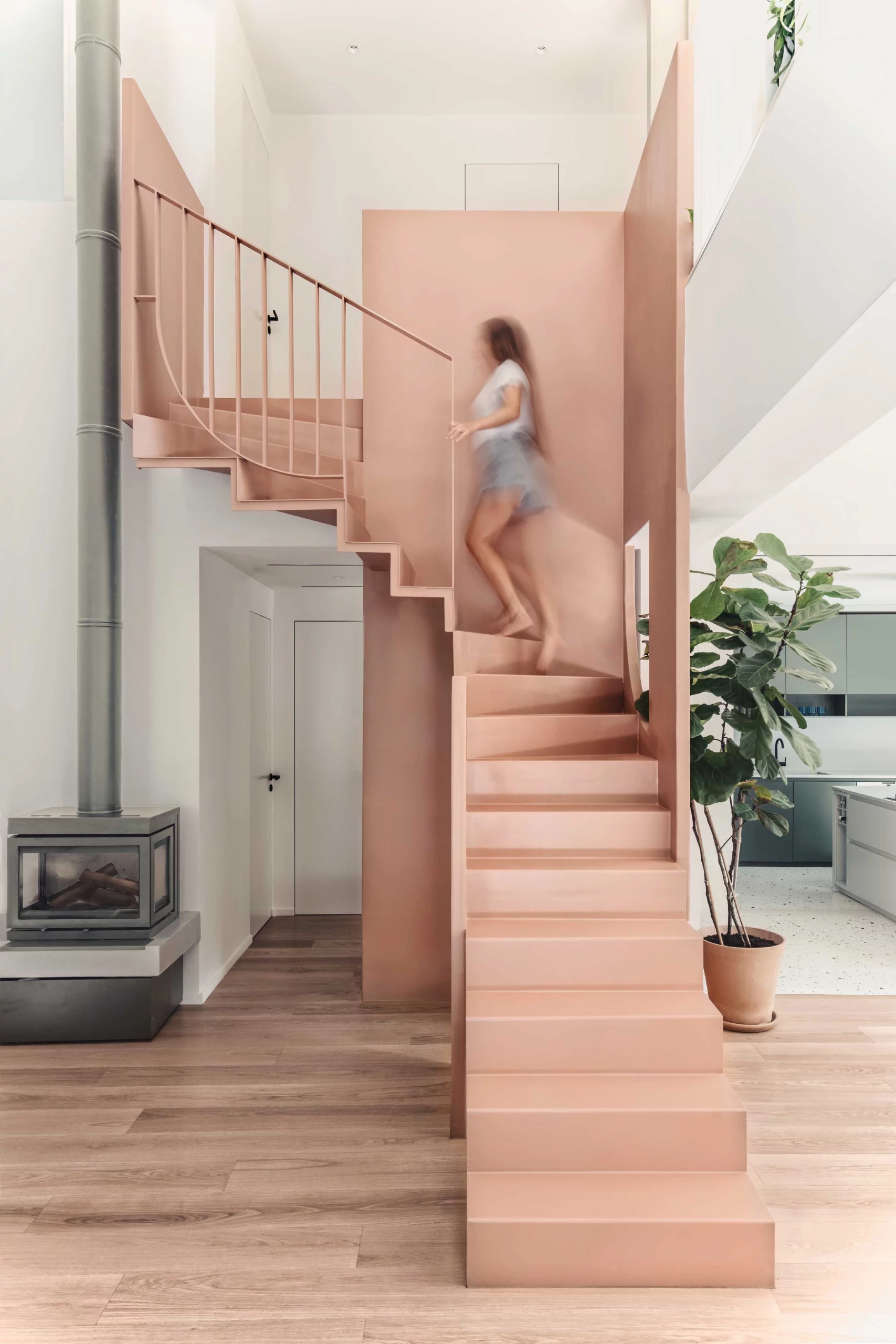 Interior of Casa D by Cometa Architects in Athens featuring a pink steel staircase, grey fireplace, and wooden floor with a blurred figure ascending