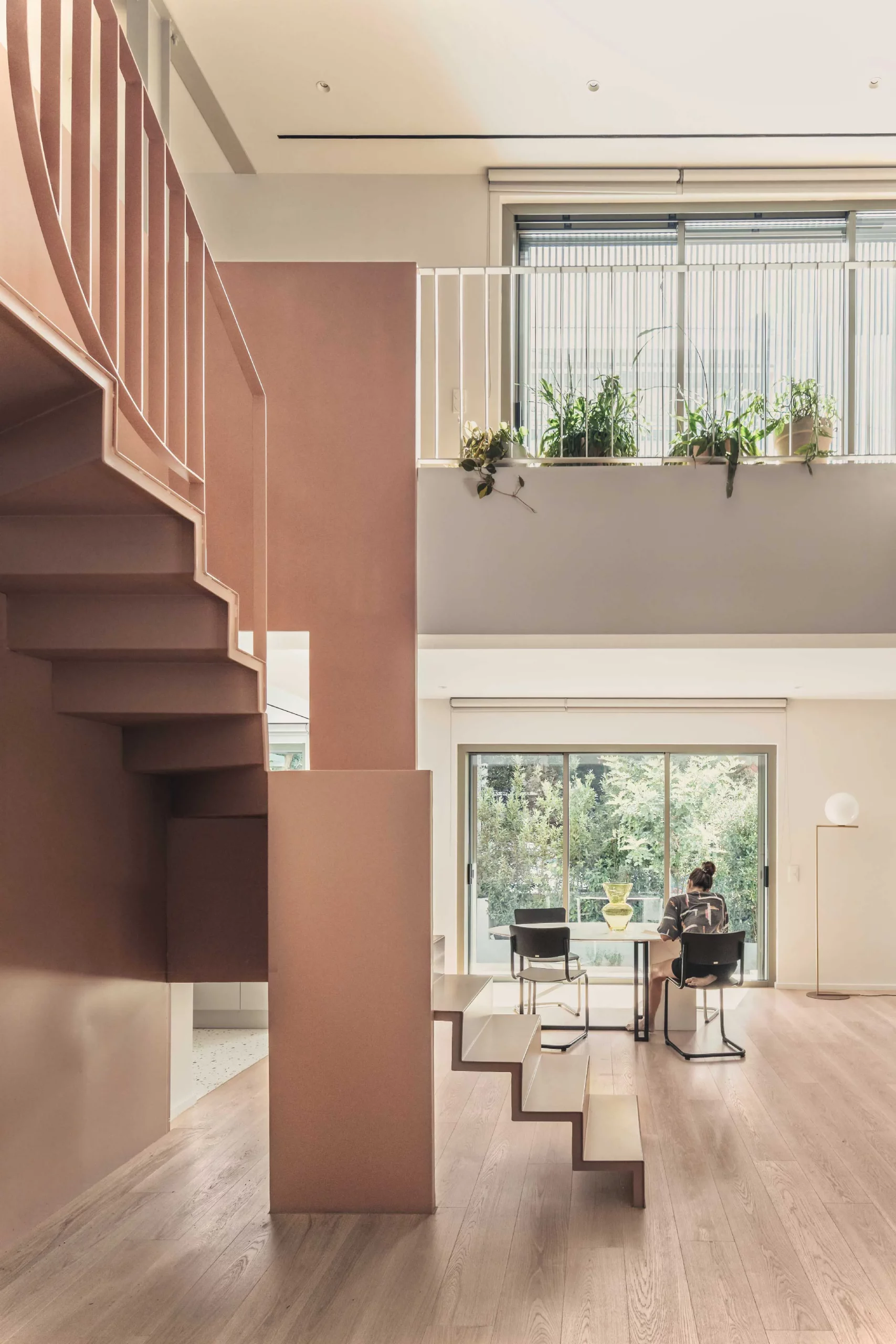 Interior of Casa D by Cometa Architects in Athens showing a pink steel staircase, wooden floor, and dining area with large windows opening to the garden.