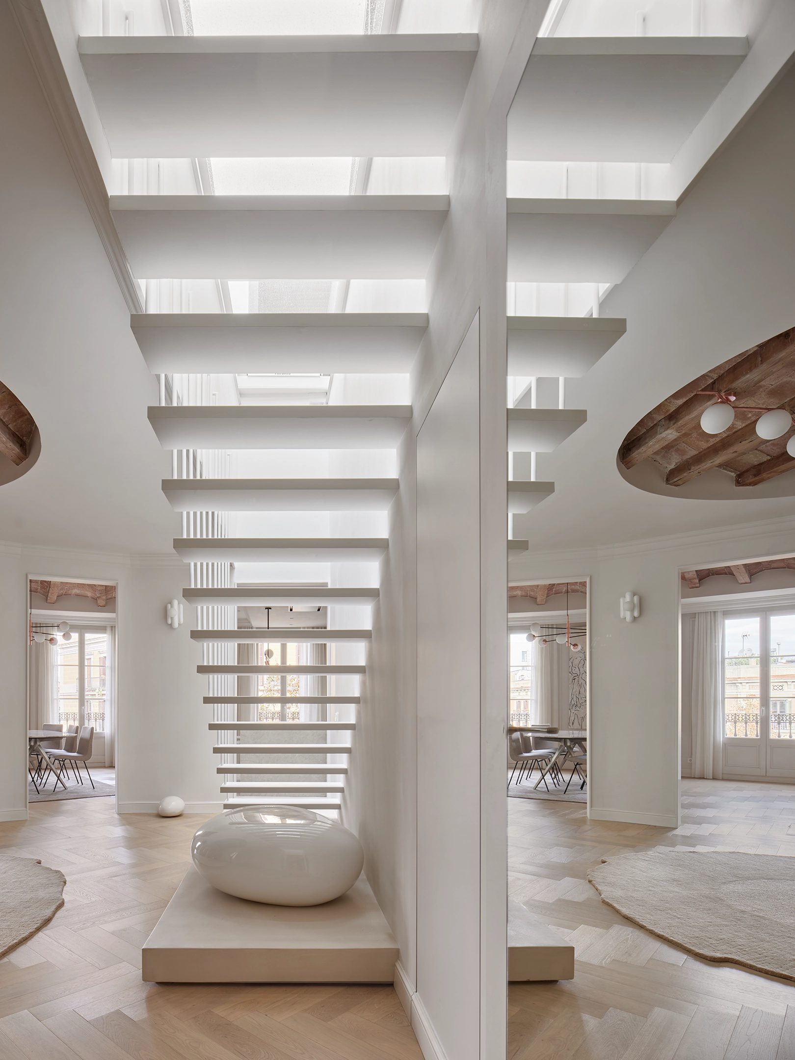 Sculptural white staircase with floating steps and natural light in a Barcelona apartment by Cometa Architects.