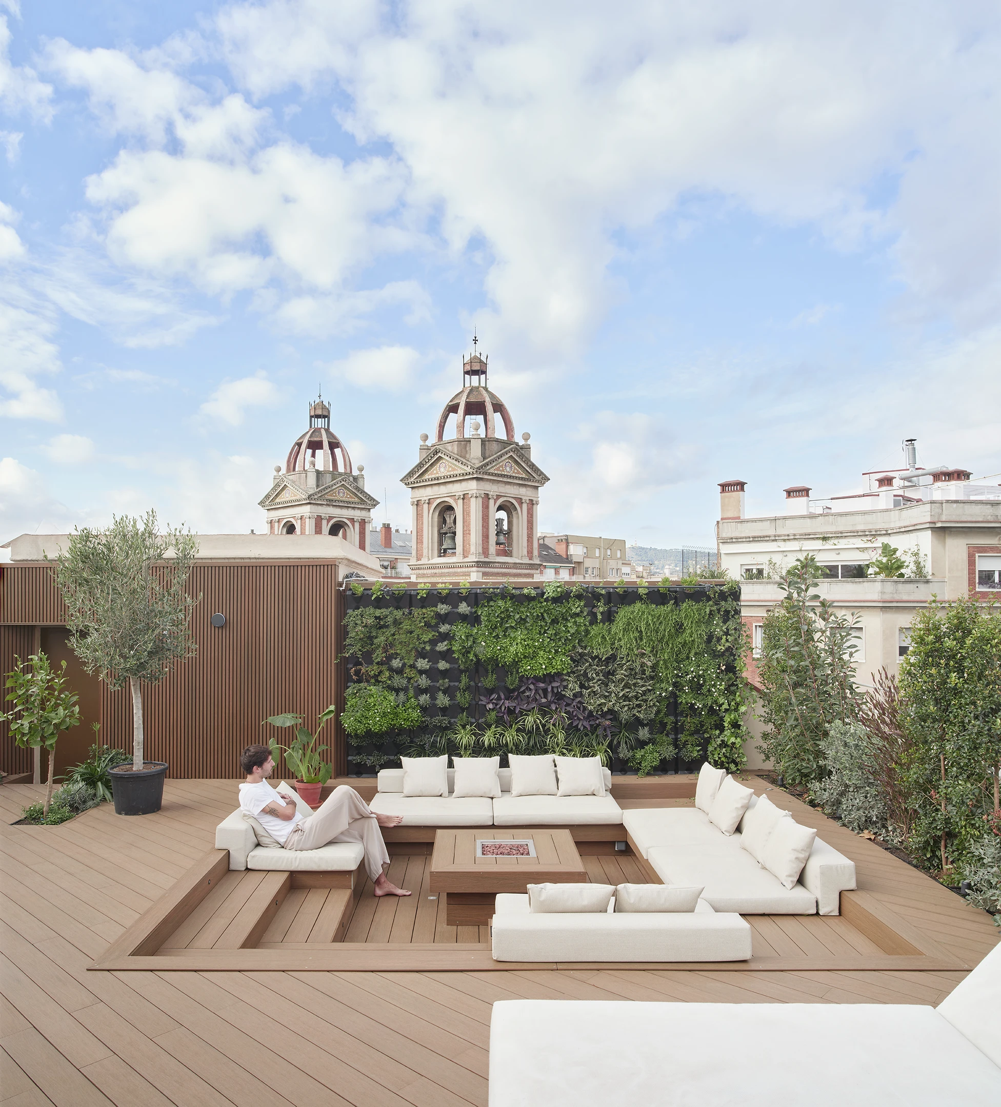 Rooftop lounge with built-in seating, vertical garden, and views of historical domes in Barcelona.