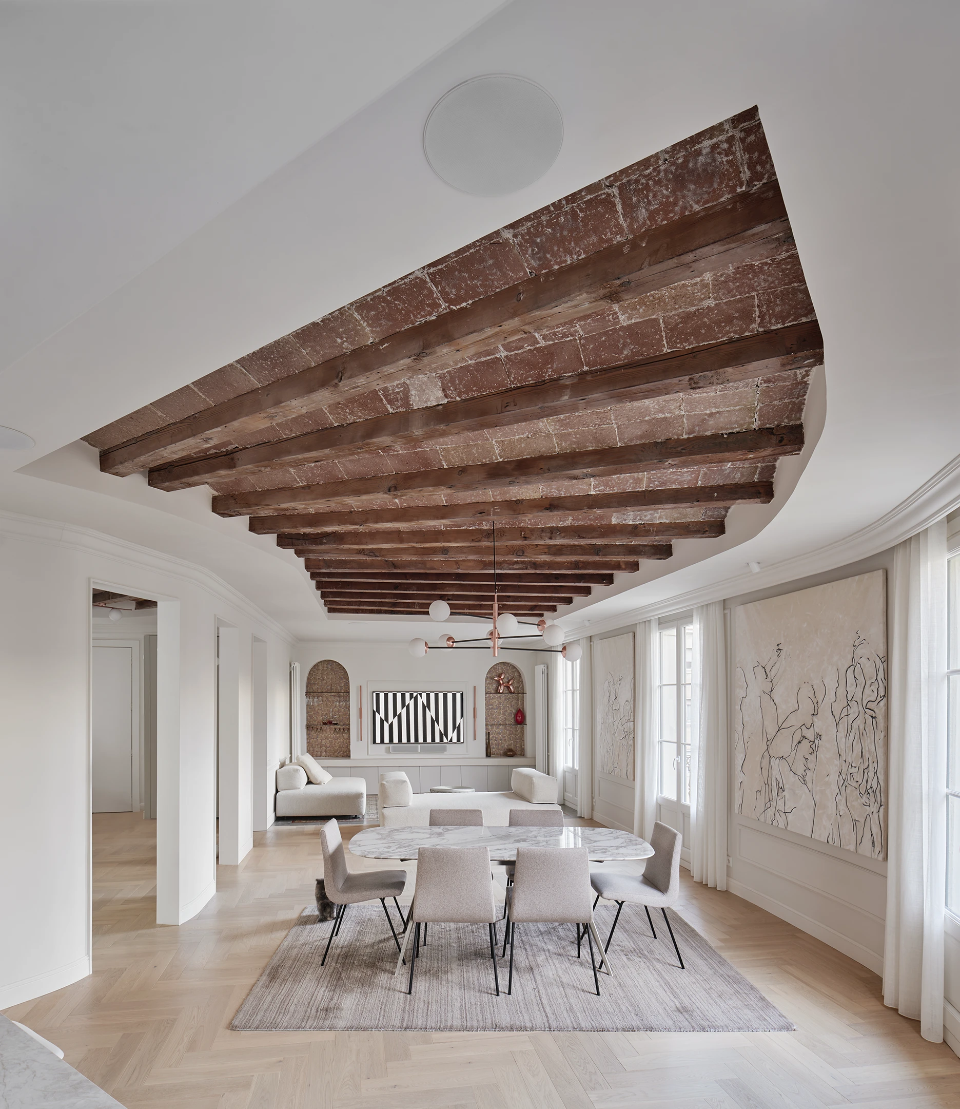 Dining area with marble table, curved walls, and original wooden beams and terracotta tiles ceiling in a Barcelona apartment.