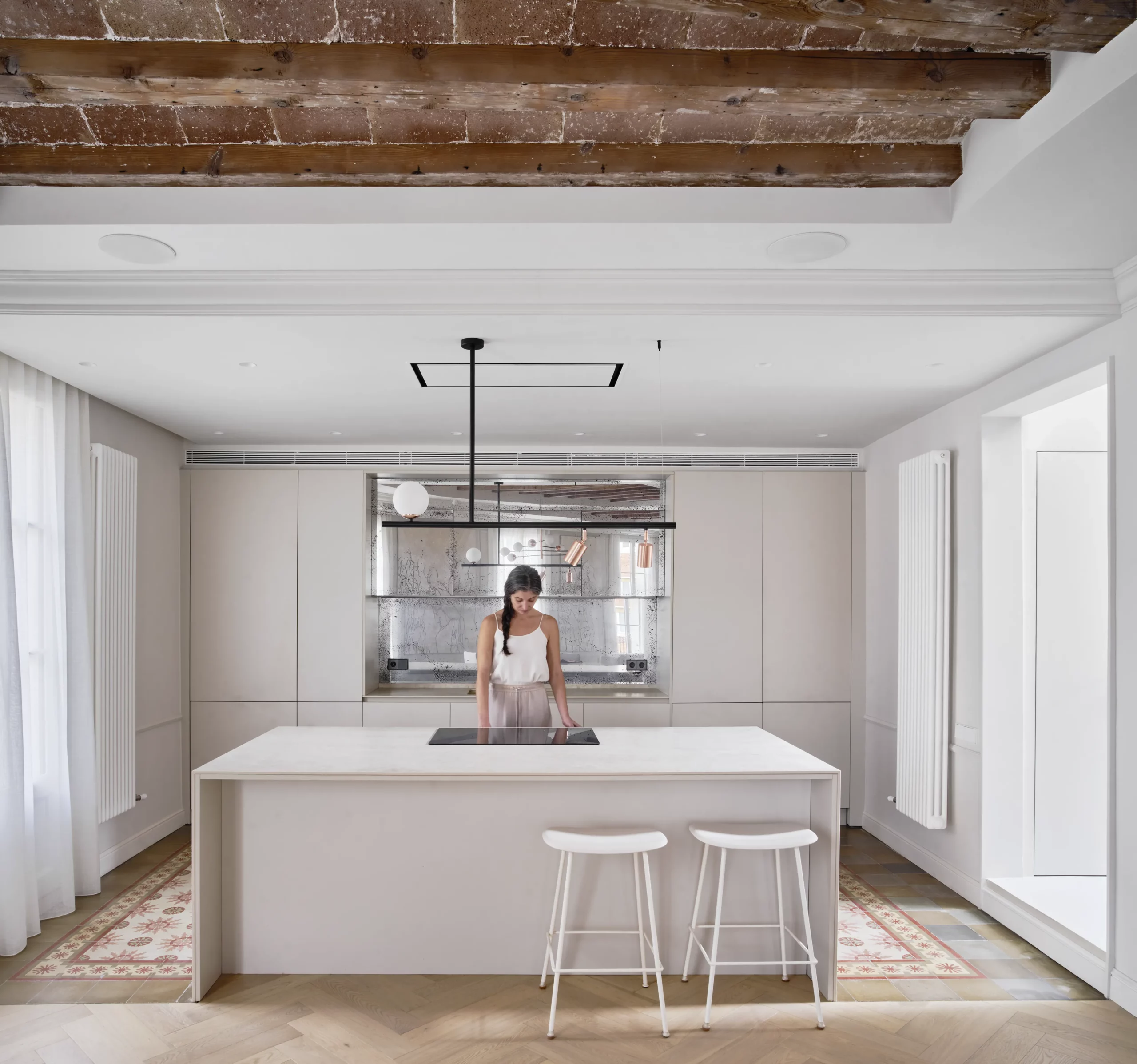 Minimalist kitchen with central island, restored hydraulic tiles, and original wooden beams and terracotta tiles in a Barcelona apartment.