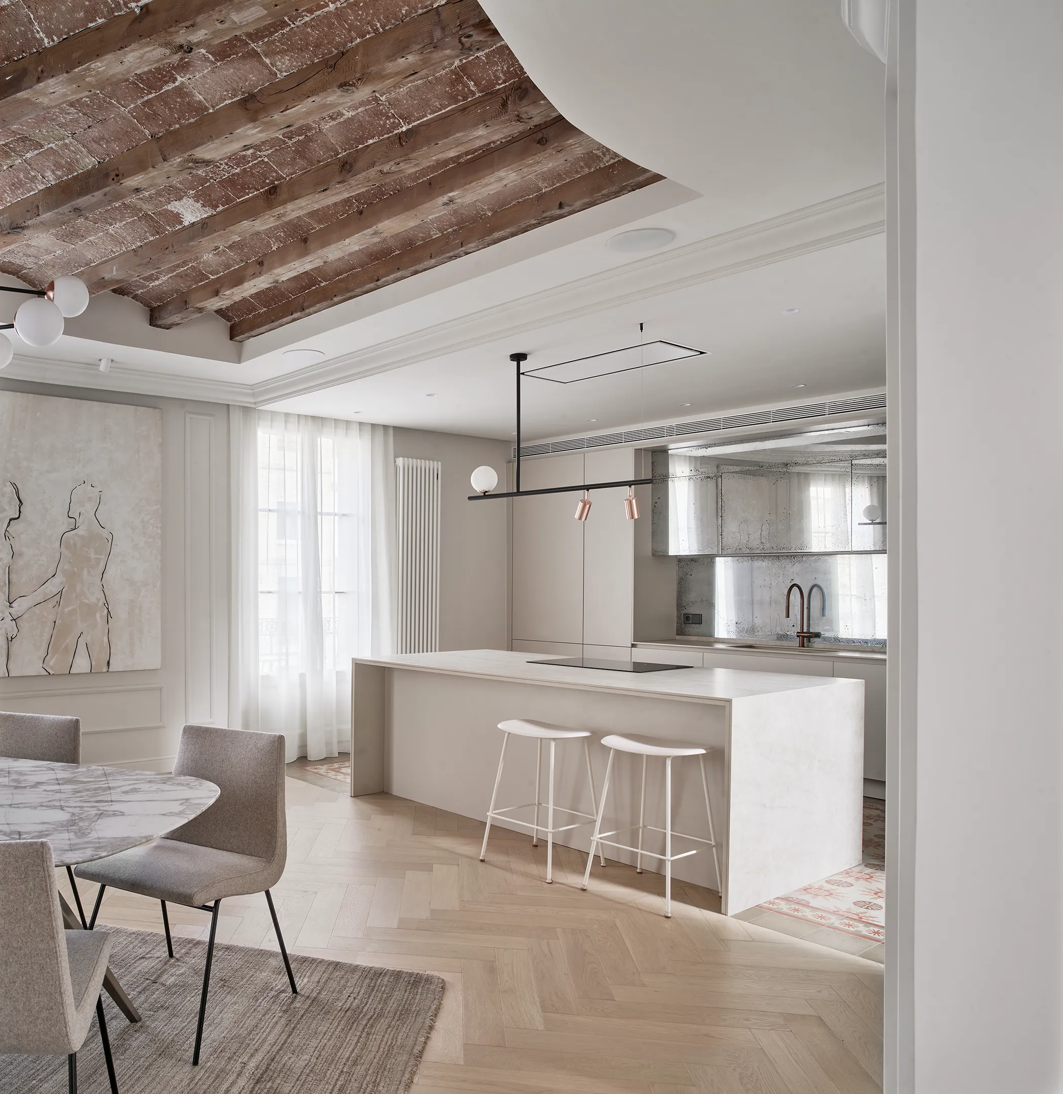 Elegant kitchen with marble dining table, mirrored backsplash, and original wooden beams and terracotta tiles in a Barcelona apartment.