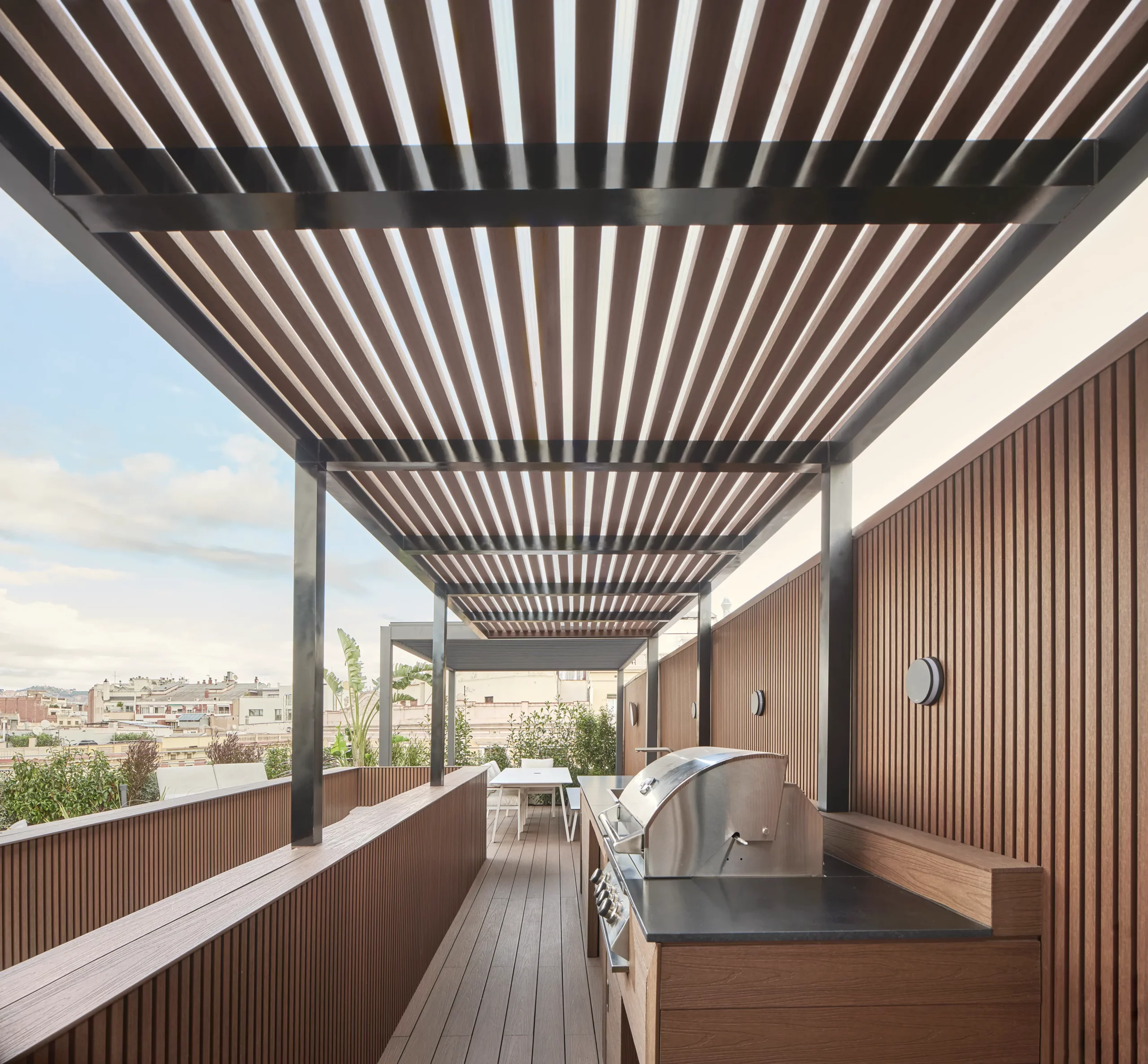 Rooftop outdoor kitchen with wooden slatted pergola, built-in barbecue, and dining area in a Barcelona apartment.