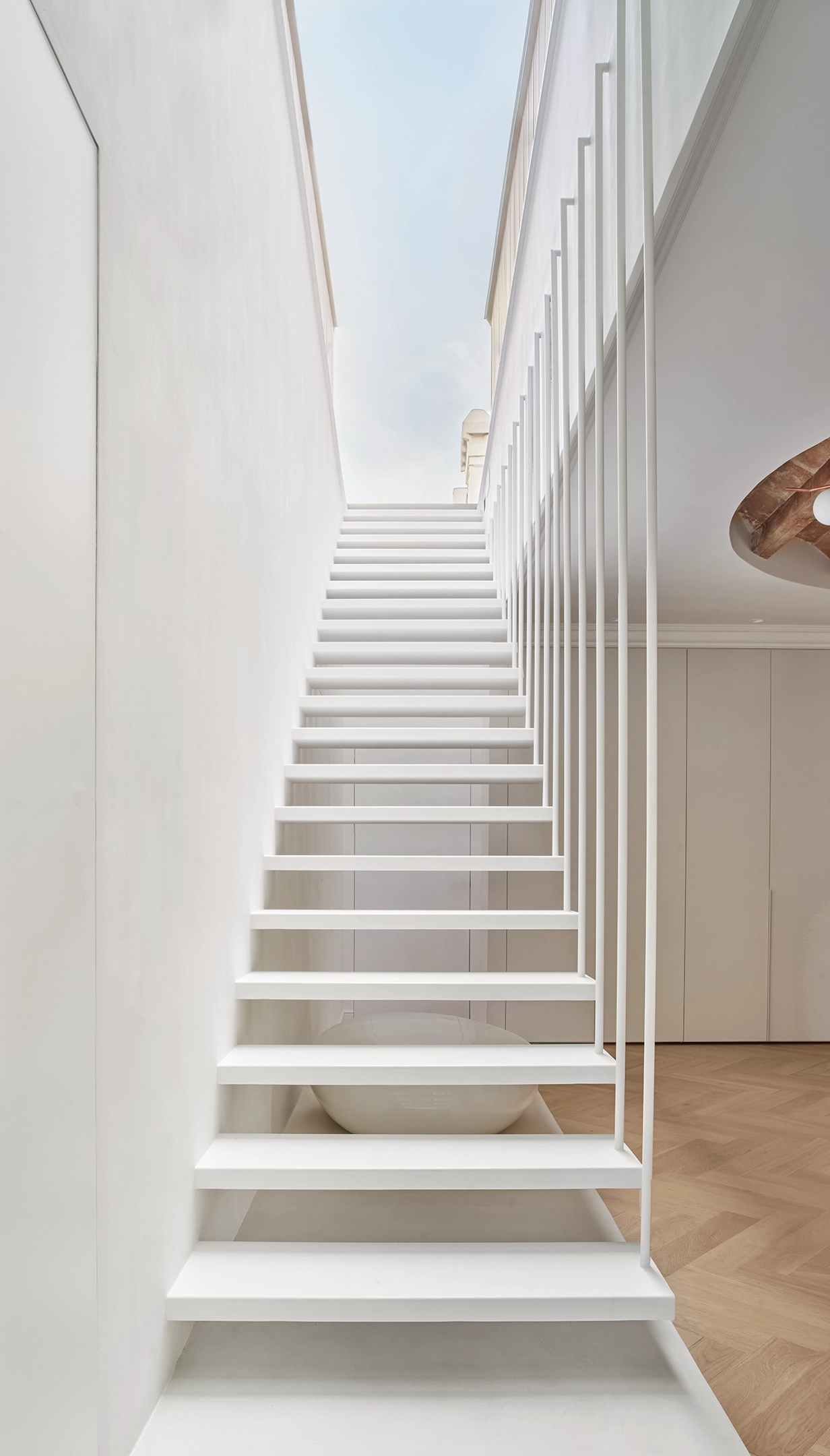 Minimalist floating staircase ascending toward a skylight in a Barcelona apartment designed by Cometa Architects.