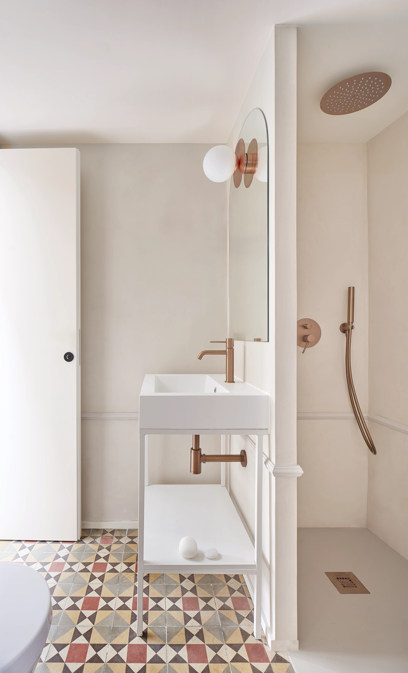 Guest bathroom with geometric hydraulic tiles, white vanity, and copper fixtures in a Barcelona apartment.