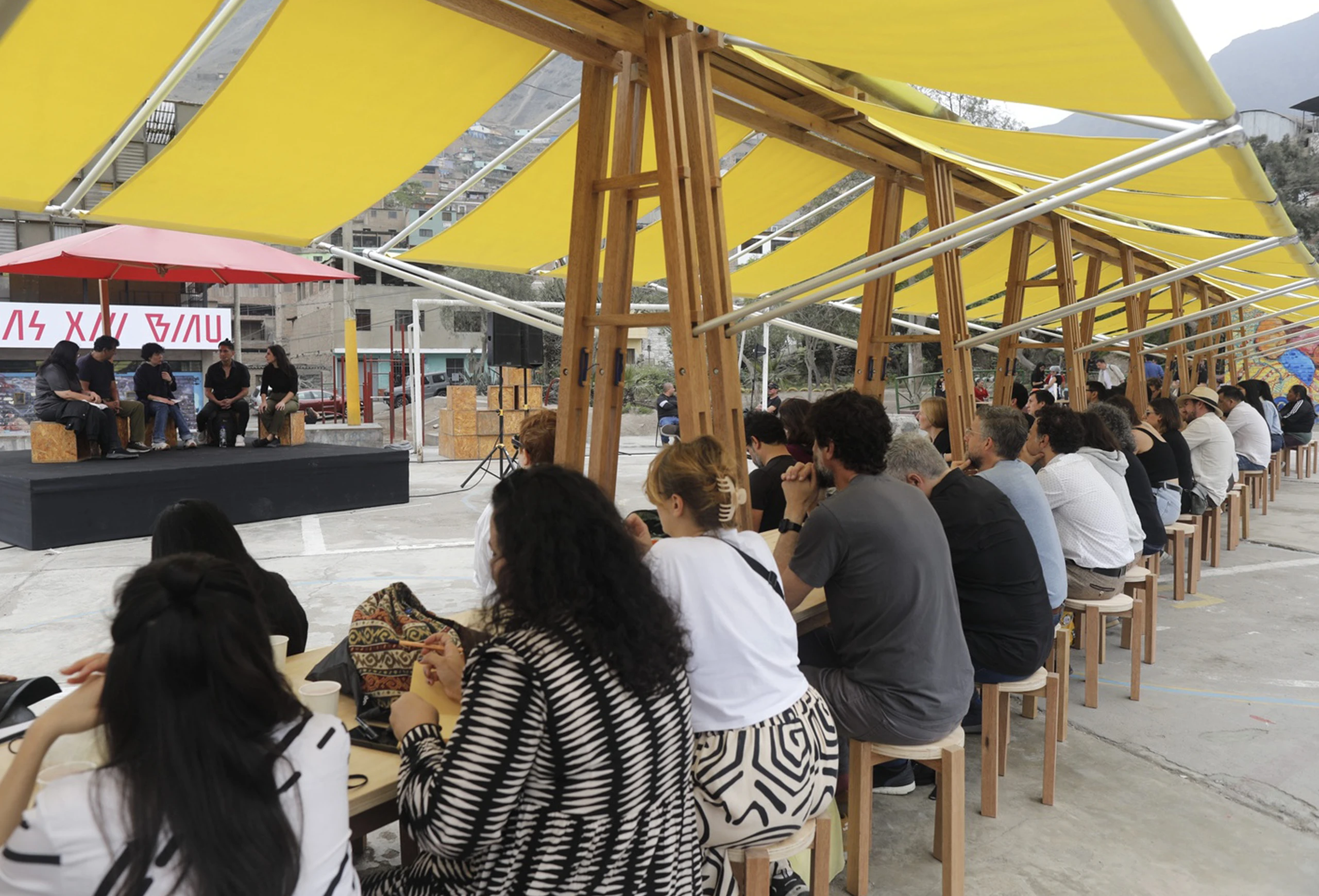 Audience and speakers under modular yellow canopy at BIAU XIII architecture event in Lima.