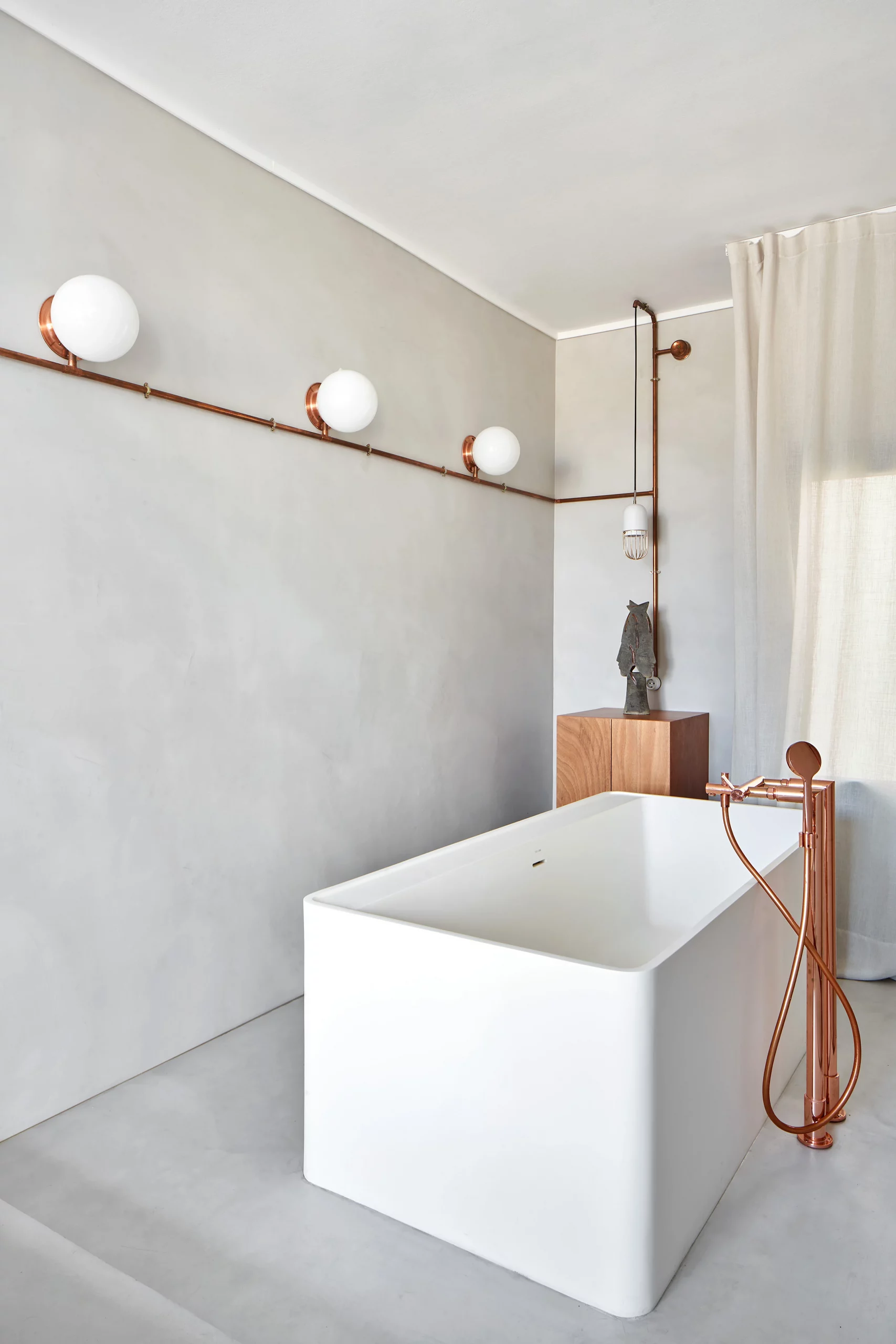 White freestanding bathtub with copper fixtures and microcement walls by Cometa Architects in Barcelona, featured in Arquitectura y Diseño magazine