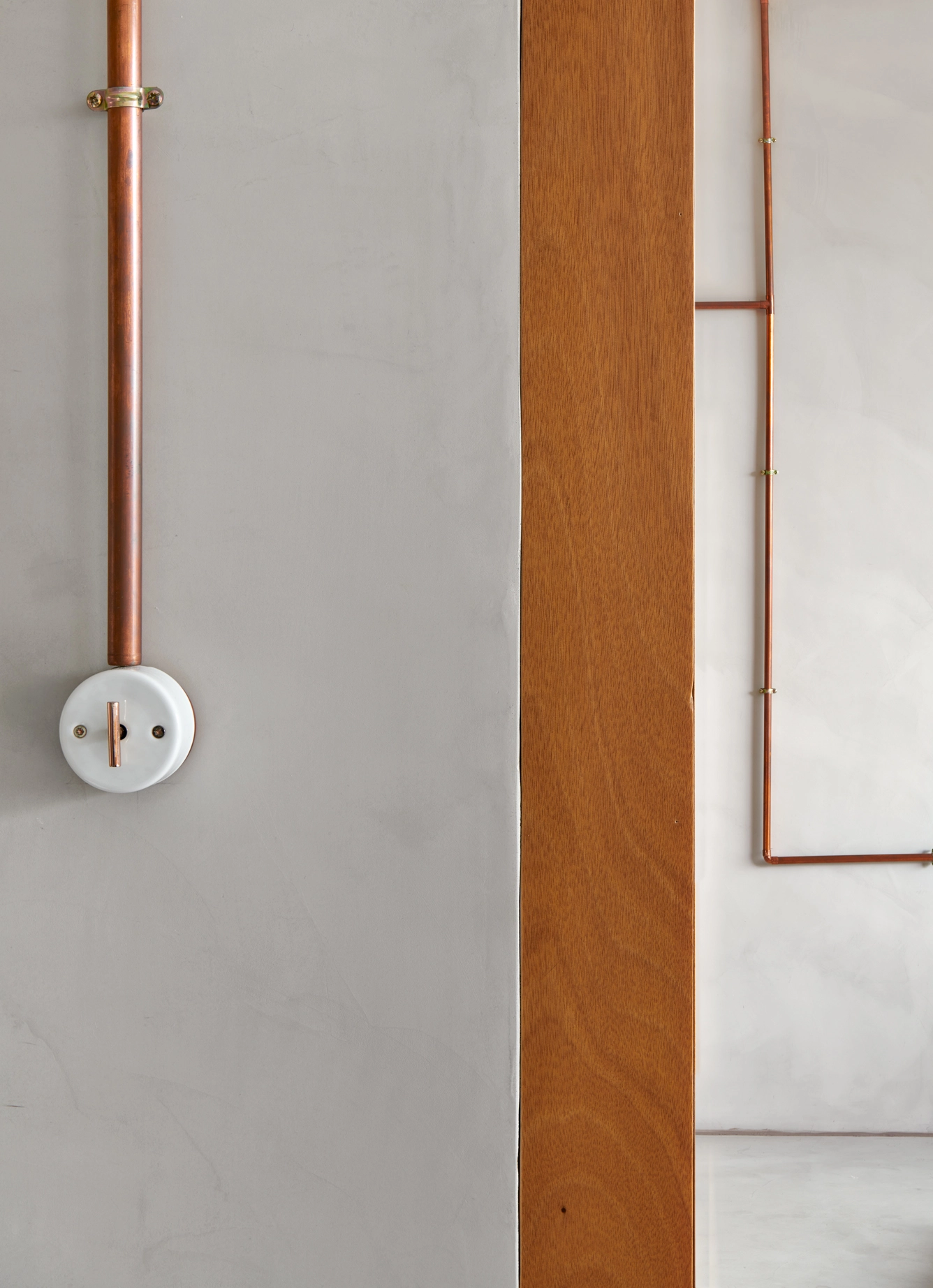 Detail of copper switch and microcement wall with wooden panel by Cometa Architects in Barcelona, featured in Arquitectura y Diseño magazine