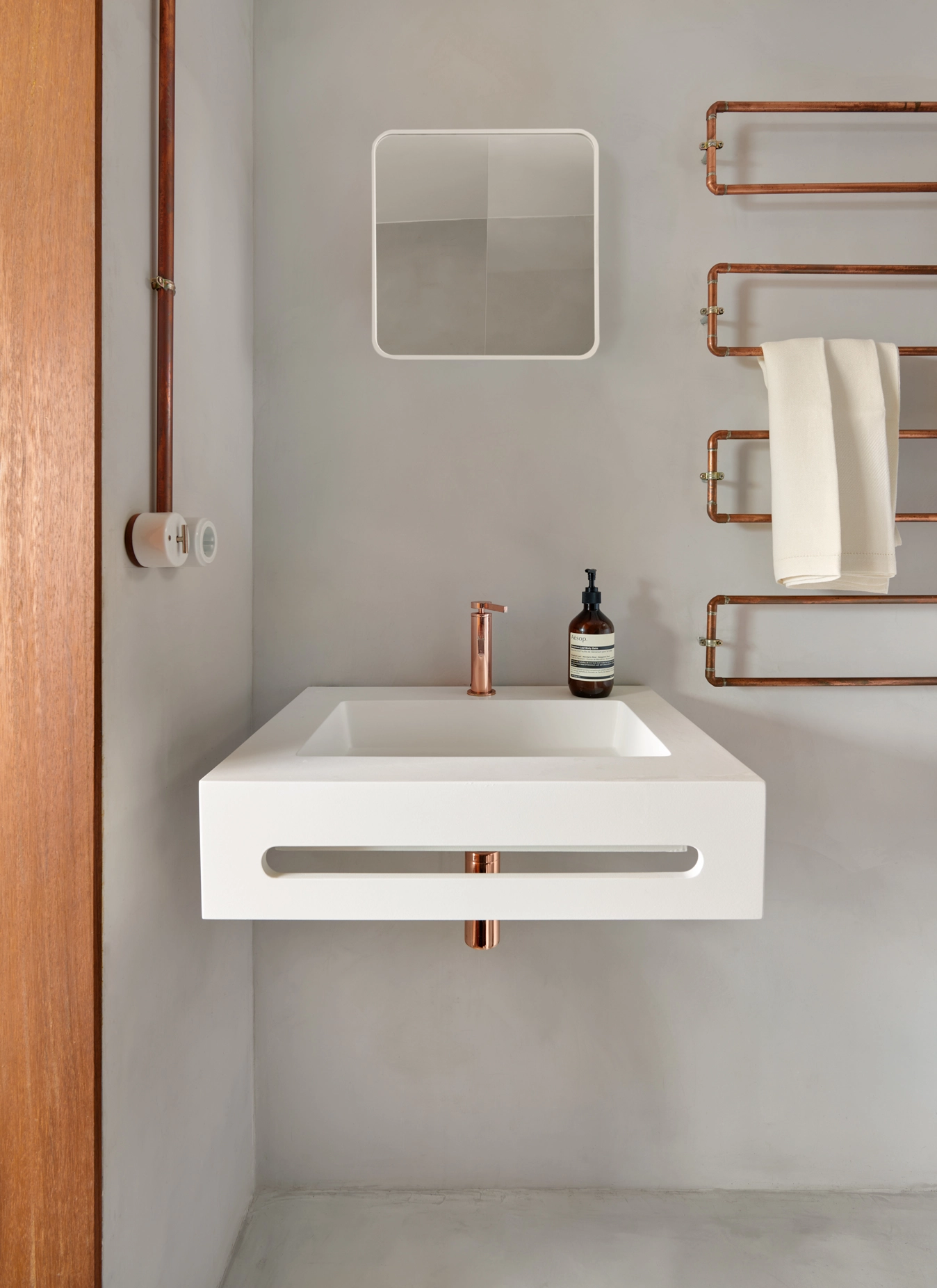 Minimalist bathroom sink with copper faucet and towel rail against microcement walls by Cometa Architects in Barcelona, featured in Arquitectura y Diseño magazine