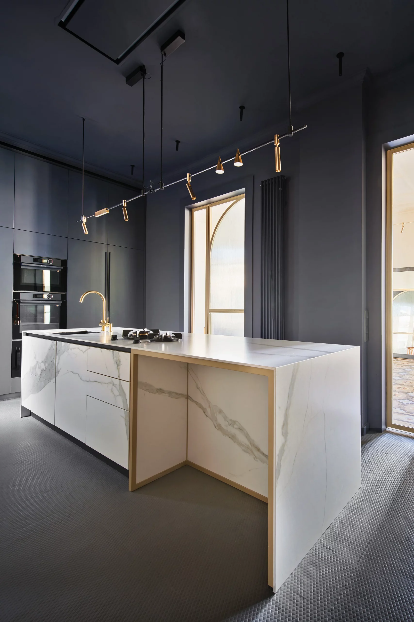 Monolithic kitchen island in Calacatta Gold marble with integrated brass detailing and dark cabinetry by Cometa Architects.