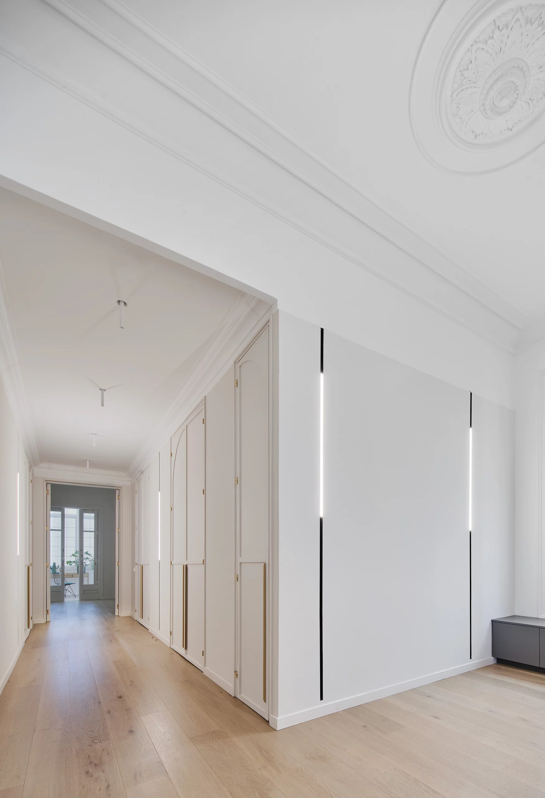 Bright corridor with oak wooden floors, custom storage cabinets, and vertical light strips designed by Cometa Architects.