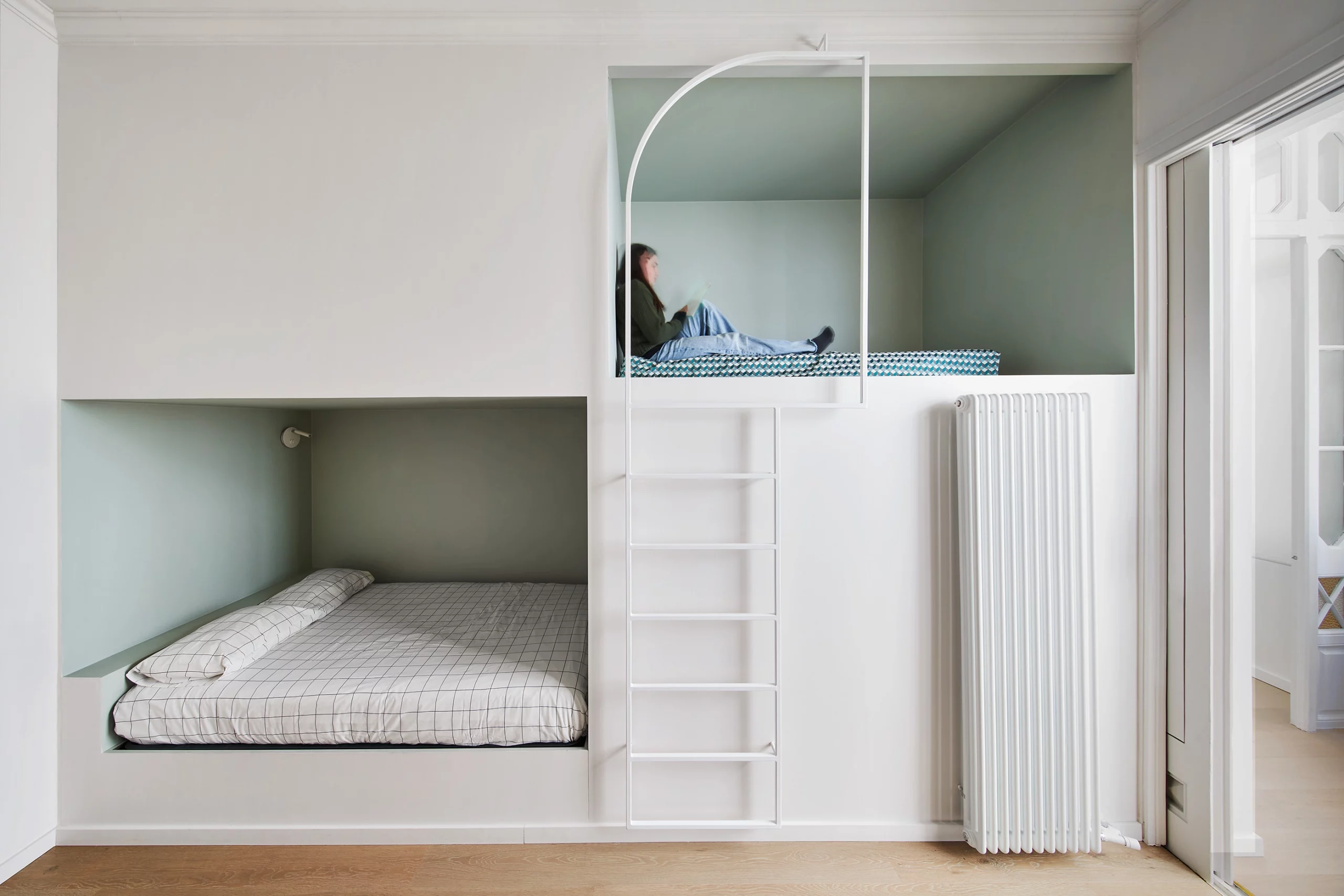 Custom-built children’s bedroom with stacked sleeping pods and a ladder in soft green tones by Cometa Architects.