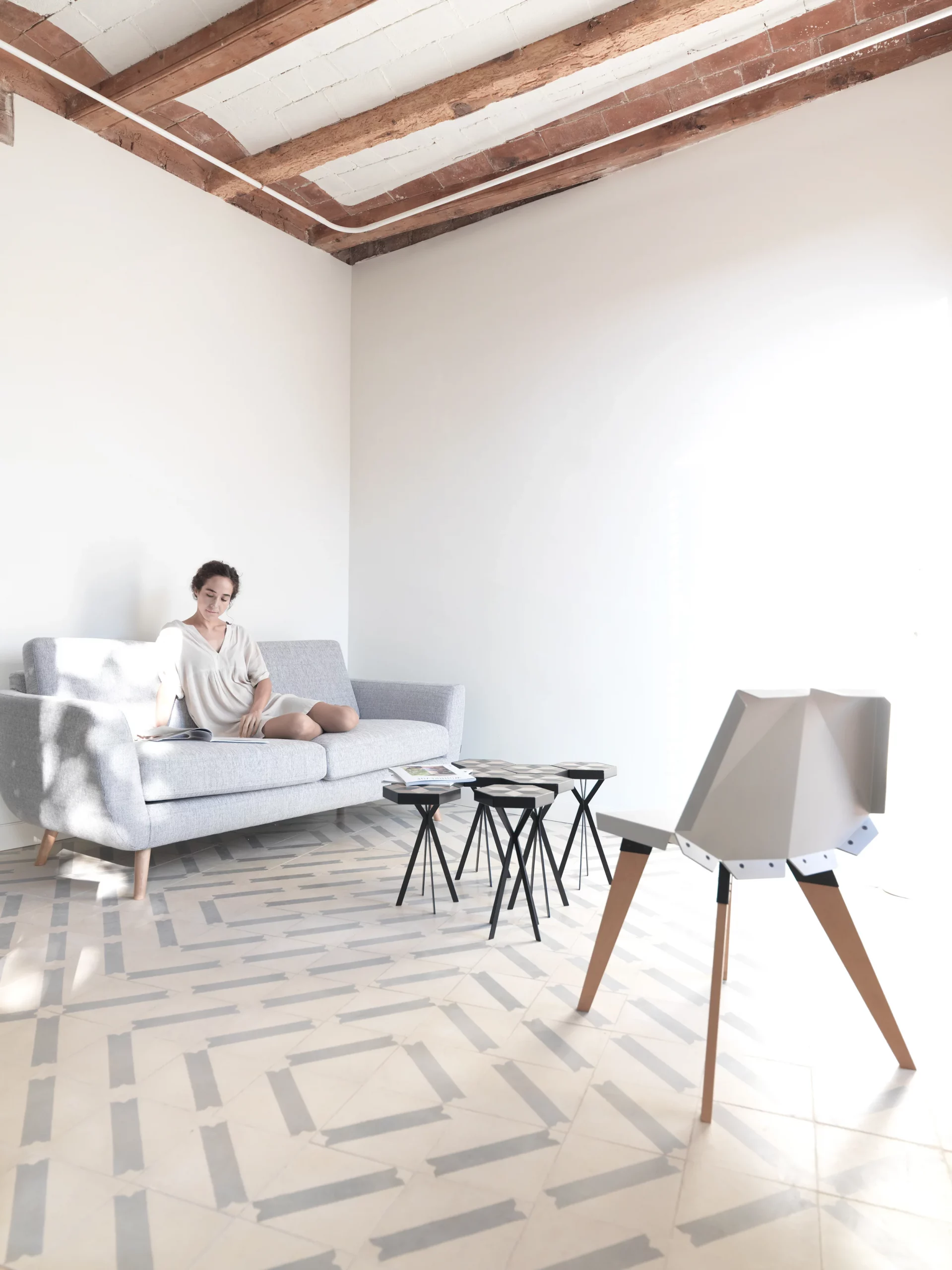 Bright living room with grey sofa, geometric chair, and patterned hydraulic tiles in The Lightslice apartment by Cometa Architects