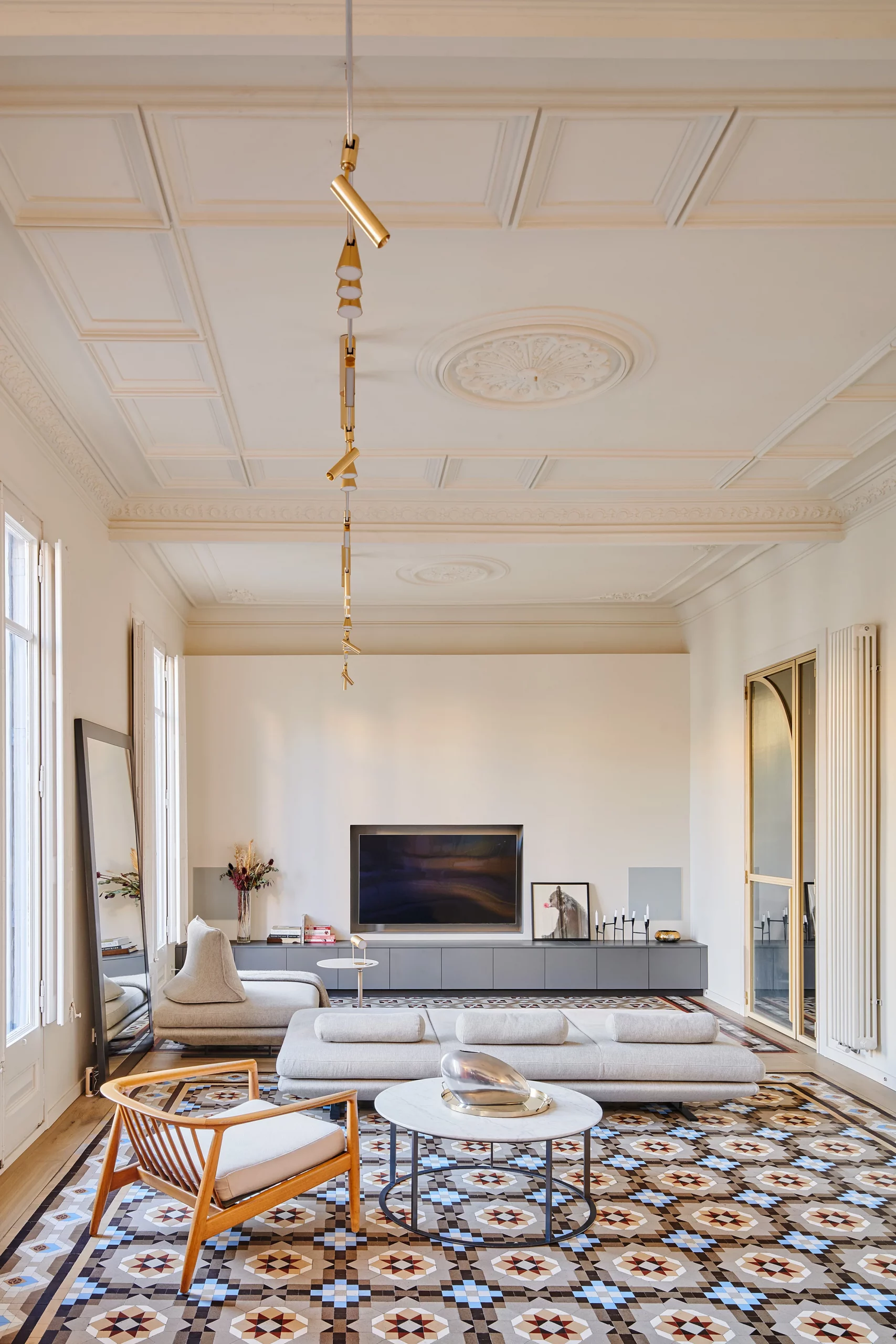 Living room with geometric patterned flooring, modern grey furniture, and brass lighting by Cometa Architects.