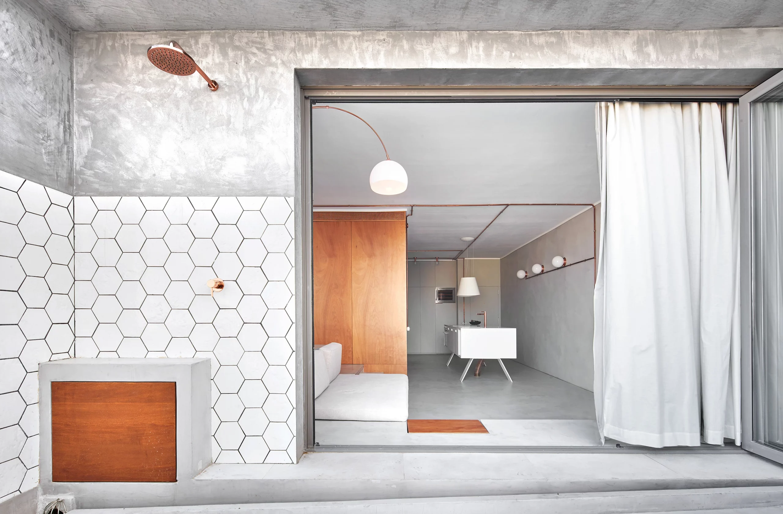 View of Marina Apartment by Cometa Architects showing the outdoor shower with hexagonal tiles and the seamless transition between terrace and microcement interior in Barcelona