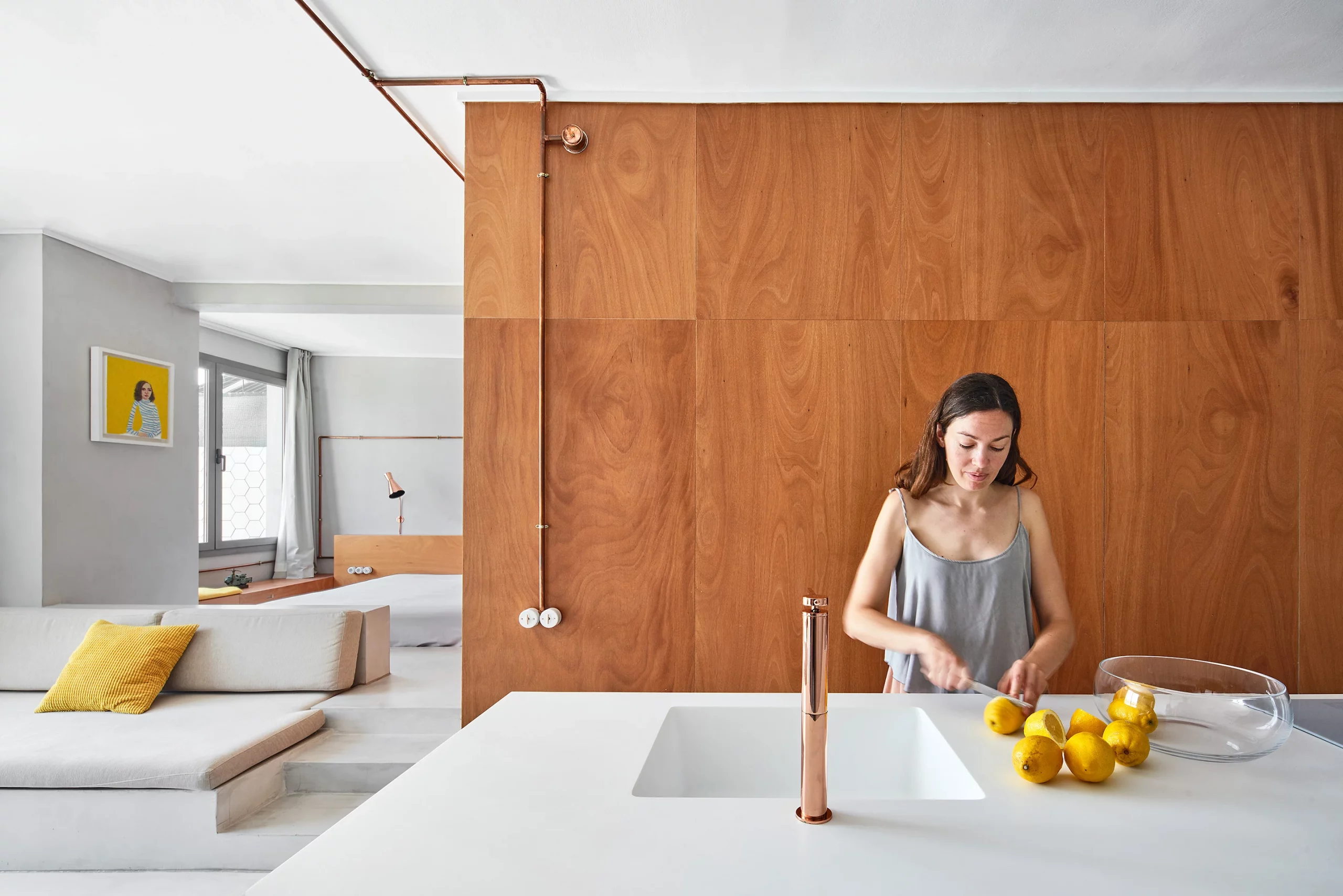 Kitchen island with copper faucet and wooden wall opening to living and bedroom areas by Cometa Architects in Barcelona