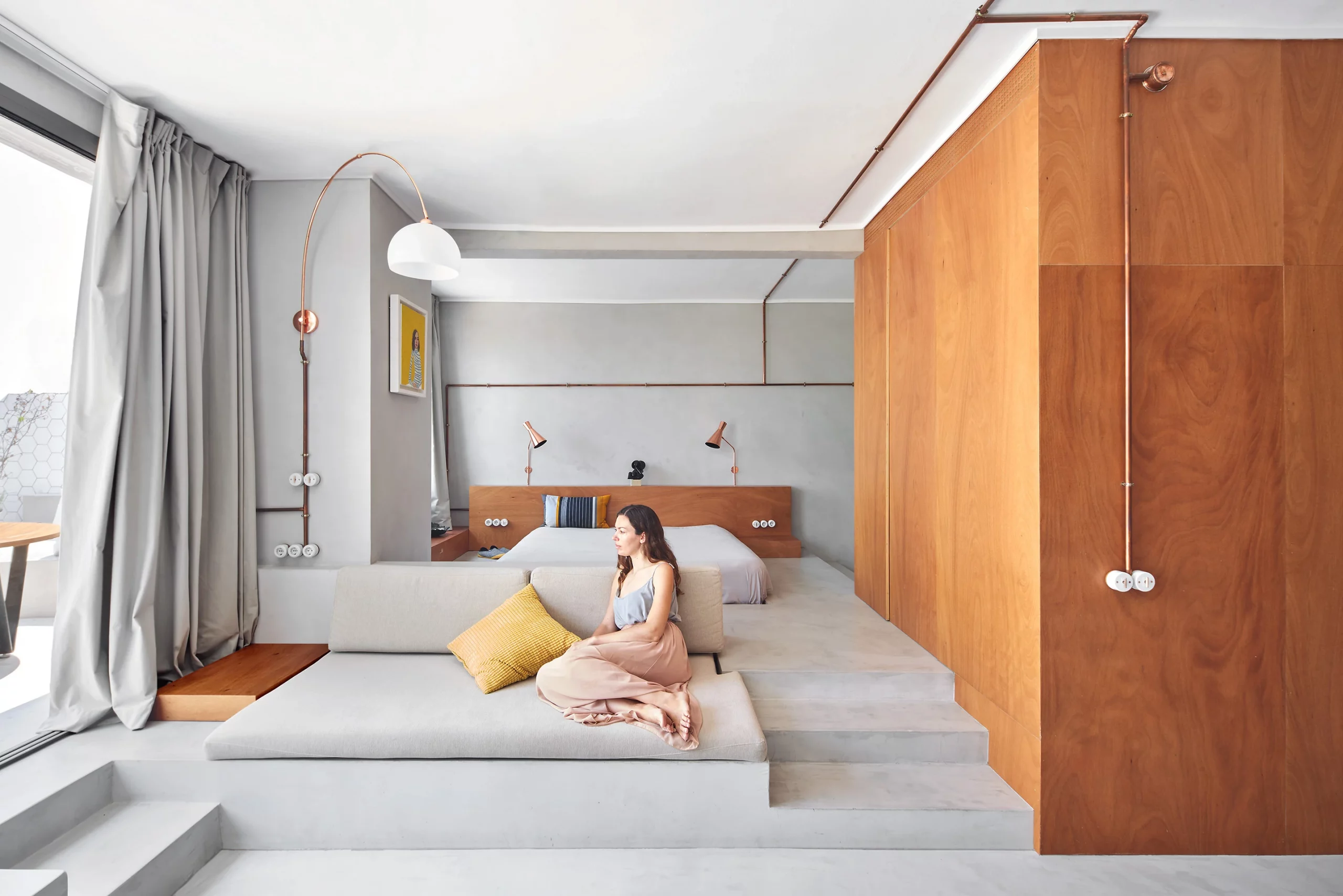 Living and bedroom area with copper lighting, wooden panels, and microcement surfaces by Cometa Architects in Barcelona