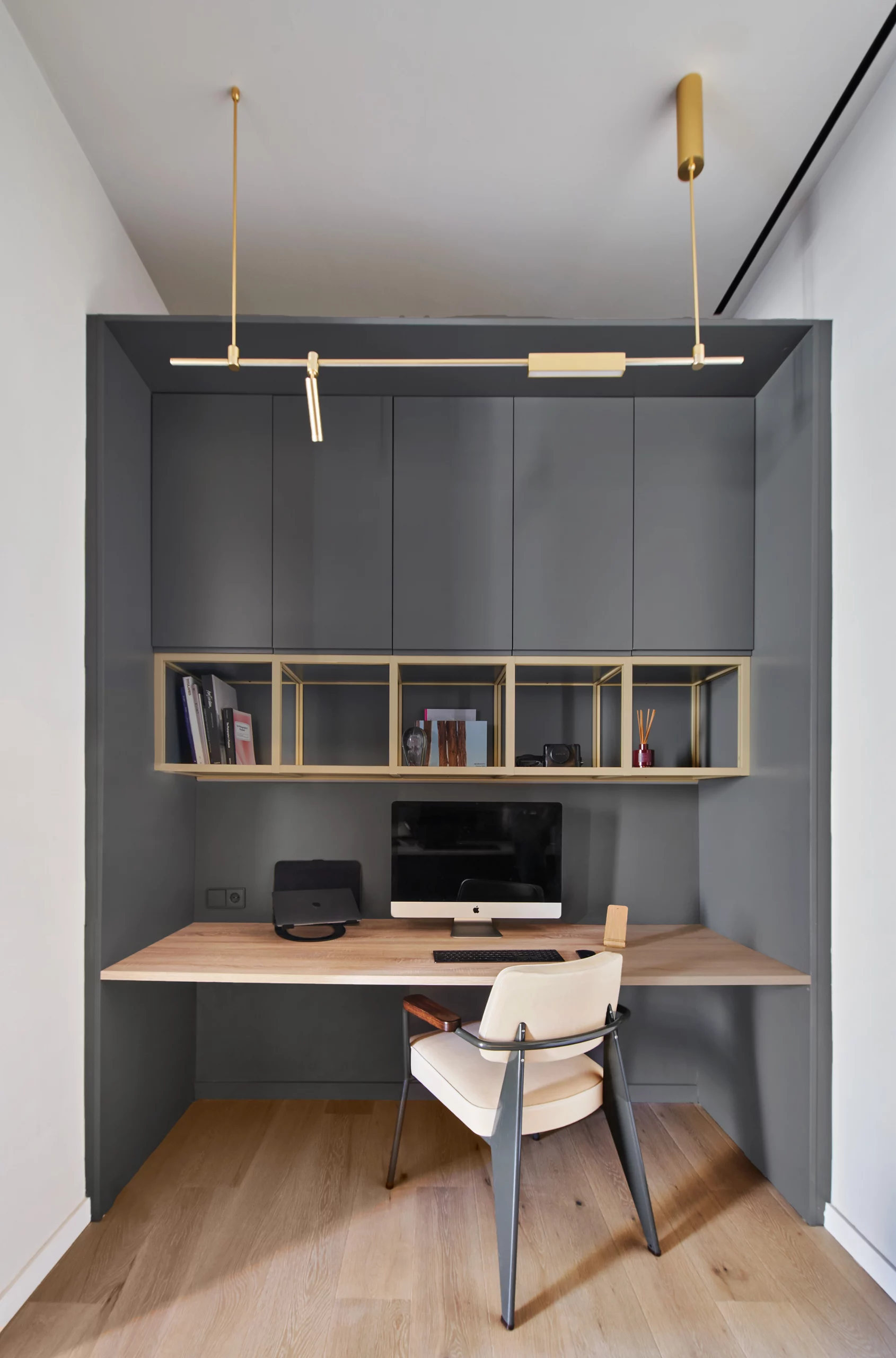 Built-in home office with dark grey cabinetry, brass shelves, and wooden desk designed by Cometa Architects.