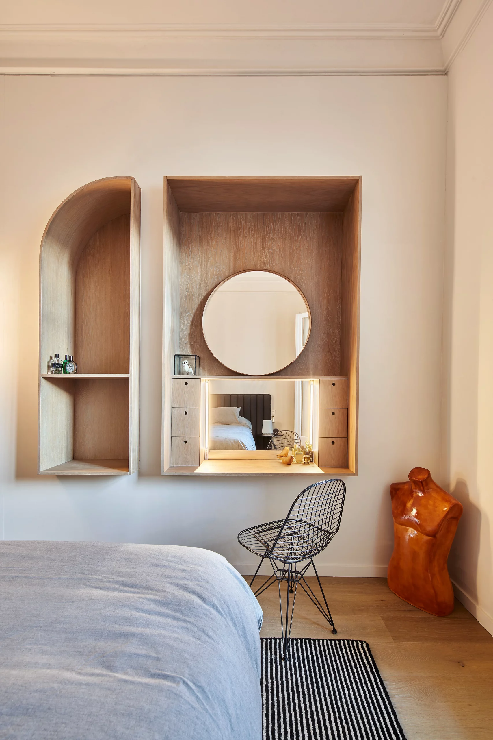 Built-in wooden vanity with circular mirror and curved shelving in a bedroom by Cometa Architects in Barcelona.