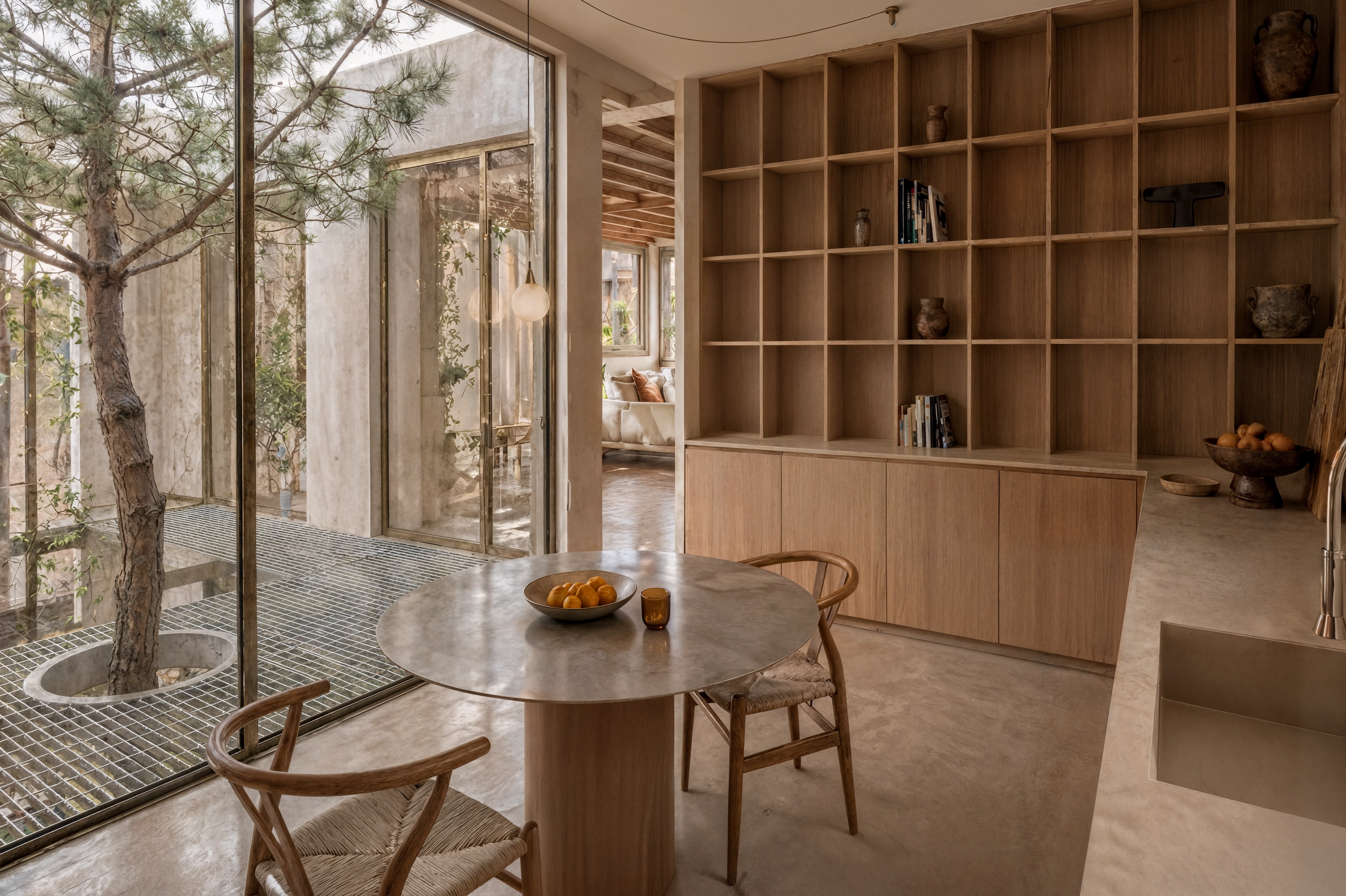 Interior kitchen of Sa Capçada in Mallorca showing timber shelving, round dining table, large glass doors, patio with pine tree, metal mesh floor and Mediterranean light.